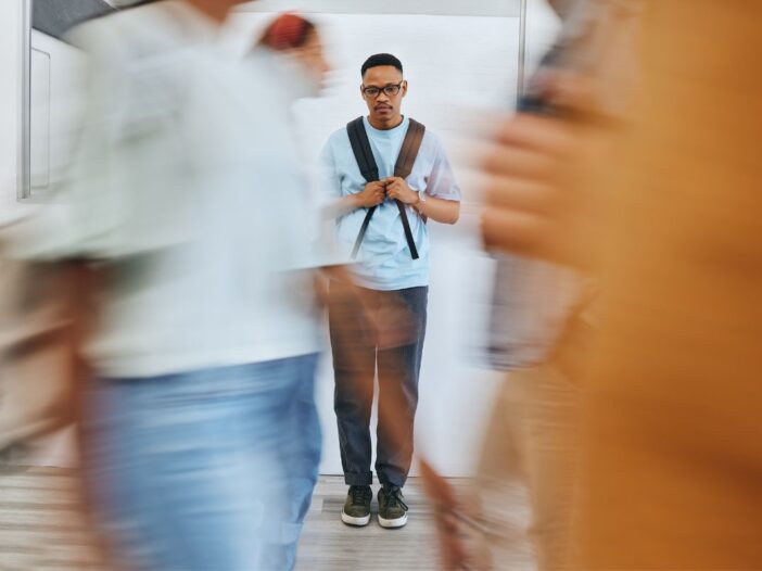 Man staat met zijn tas helemaal alleen op de wereld lijkt het. Alle mensen lopen deze man straal voorbij.