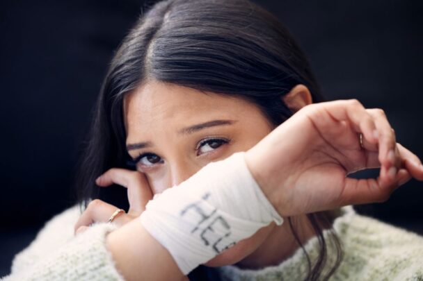 Vrouw die zichtbaar verdrietig is en op zoek is naar hulp. Dat kan je zien daar het verband wat ze draagt met 'help' erop.