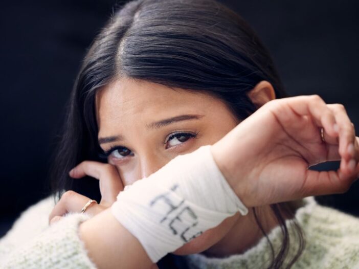 Vrouw die zichtbaar verdrietig is en op zoek is naar hulp. Dat kan je zien daar het verband wat ze draagt met 'help' erop.