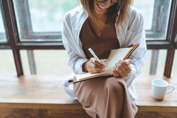 Vrouw lacht en schrijft blij in een notitieboek