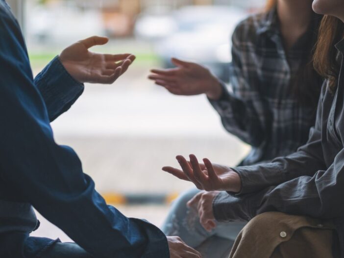 Drie personen zitten bij elkaar. Ze bewegen met hun handen naar elkaar