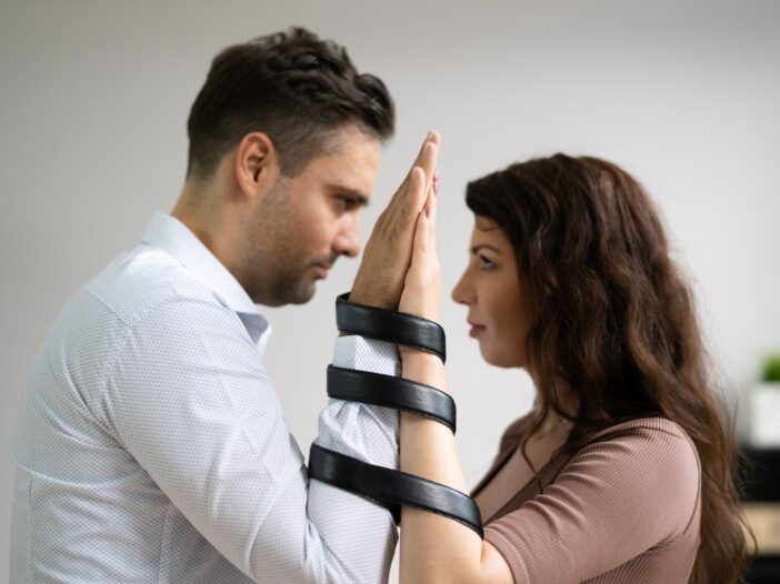 Een man en vrouw zijn vastgebonden aan hun polsen. Ze kijken elkaar aan.