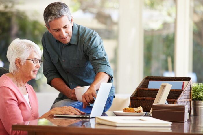 Man wijst iets aan op een laptop. Een oudere vrouw kijkt naar de laptop.