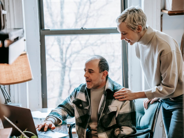 Vrouw en man kijken samen naar computerscherm, de vrouw lacht