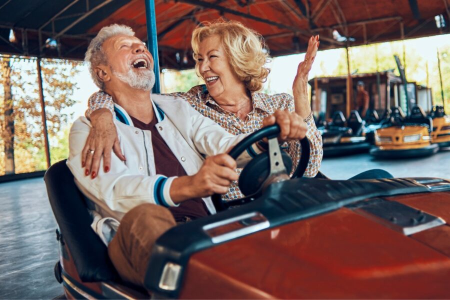 Oudere man en vrouw zitten samen in een botsauto en lachen breed