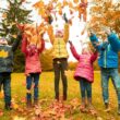 Vijf kinderen zijn buiten in het bos. Ze gooien herfstbladeren in de lucht.