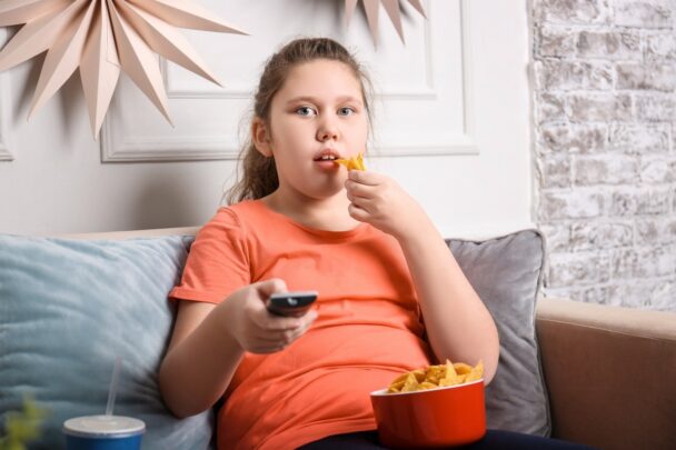 Meisje zit op de bank met een bakje chips en ze heeft een afstandsbediening in haar handen.