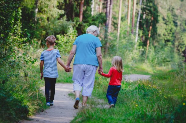 Oudere vrouw maakt met twee kleine kinderen een wandeling in een groene omgeving.