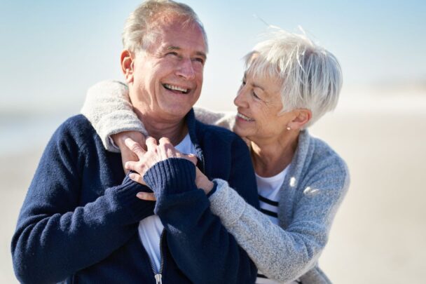 Oudere man en vrouw geven elkaar een knuffel op het strand.