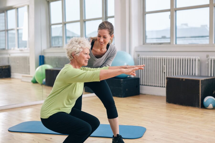 Oudere vrouw traint samen met een jongere vrouwelijke coach in een sportzaal.