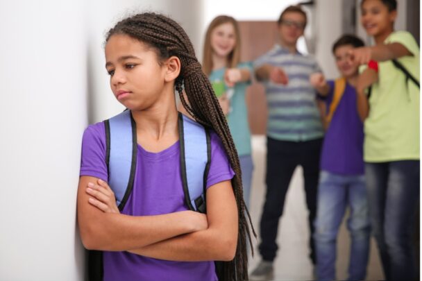 Meisje wordt gepest op school. Ze staart naar de muur en andere kinderen wijzen naar haar en lachen haar uit.