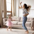 Een vrouw danst met haar dochter in hun woonkamer. Het meisje draagt een roze tutu