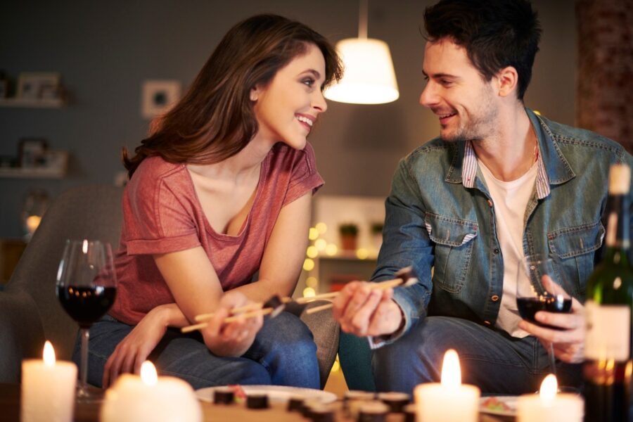 Man en vrouw hebben een date op de bank, met sushi, wijn en kaarsen.