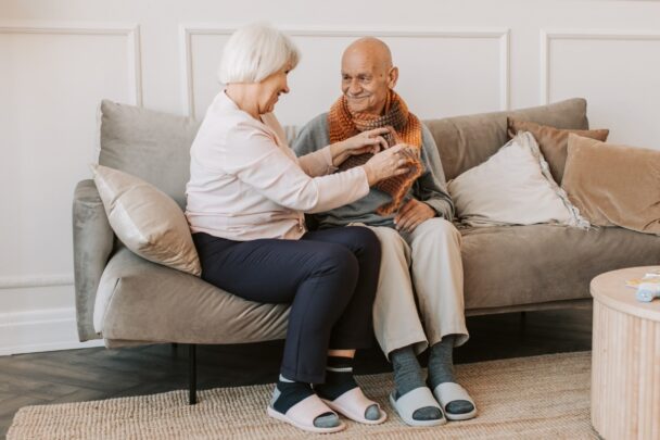 Oudere man en vrouw zitten samen op de bank en zijn in gesprek met elkaar.