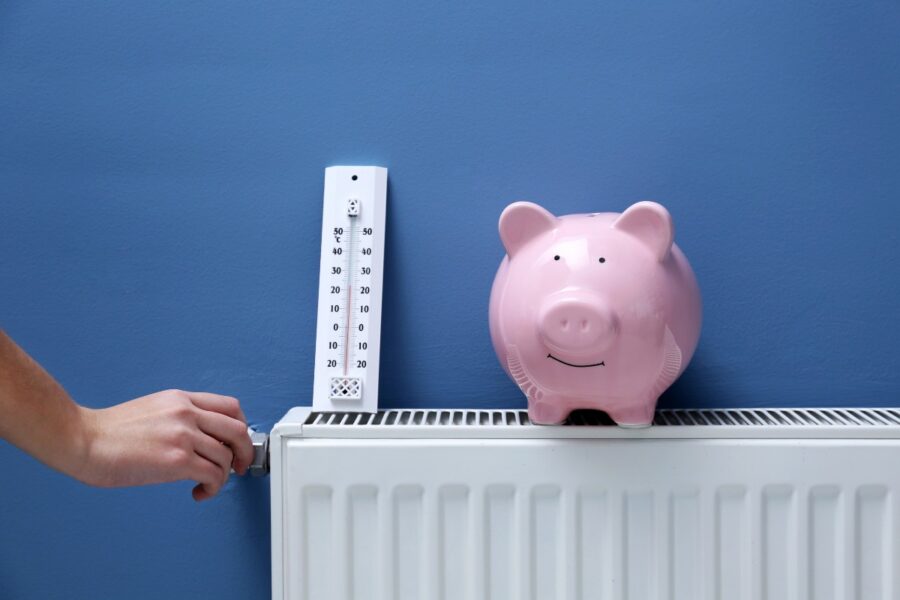 Een spaar varken op een verwarmingsradiator. Iemand draait aan de knop van de verwarming.