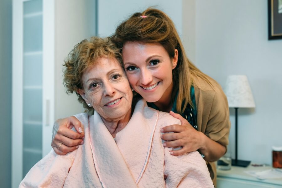 Jonge en oudere vrouw samen op de foto. De jongere vrouw houdt de andere vrouw vast als zijnde een omhelzing.