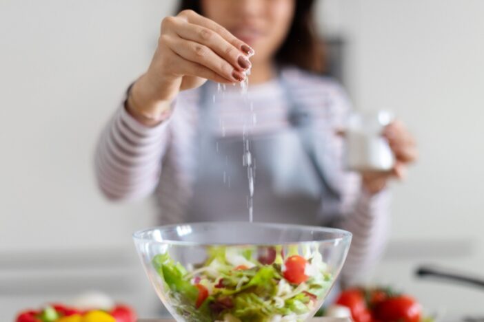 Vrouw voegt zout toe aan een schaal met salade.