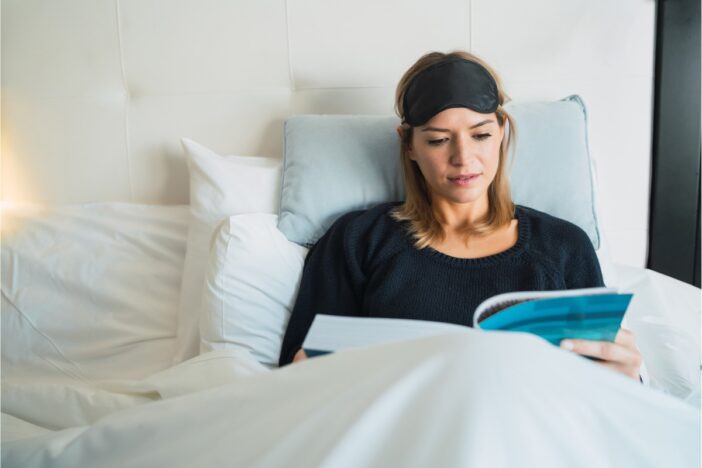Vrouw ligt in bed een boek te lezen.