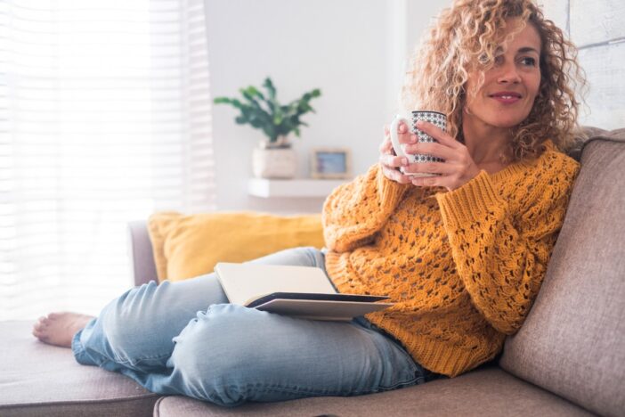 Vrouw zit ontspannen op de bank met een kopje thee.