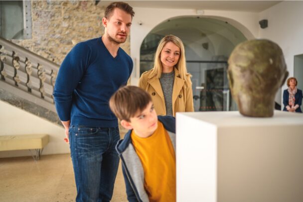Man, vrouw en kind kijken samen naar een beeld in een museum
