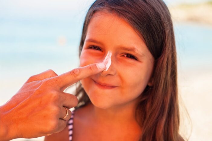 Jong meisje wordt op haar neus ingesmeerd met zonnebrand.