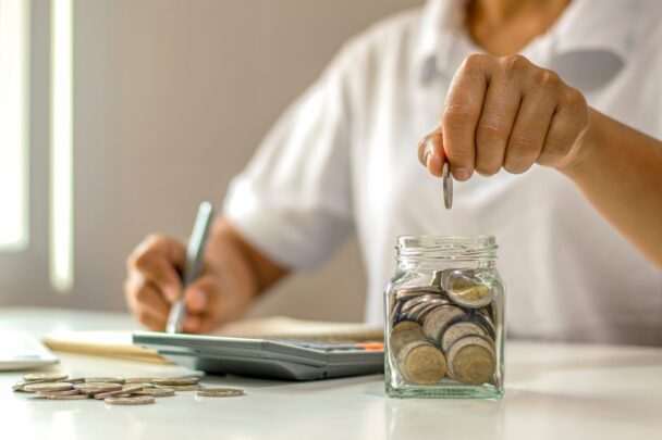 Man zit aan een tafel te rekenen en gooit muntgeld in een glazen potje.