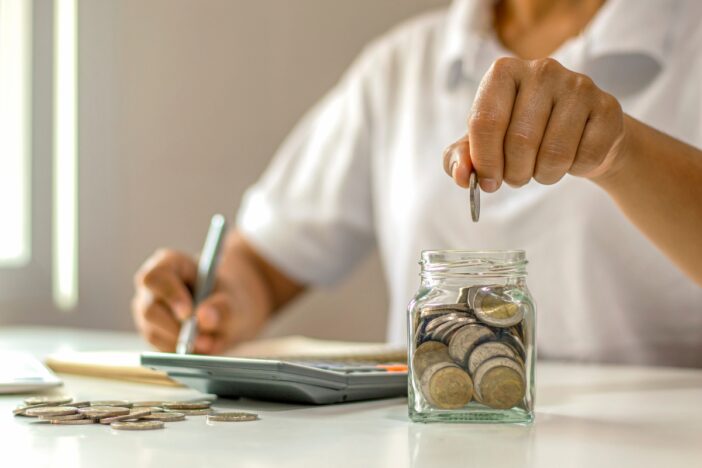 Man zit aan een tafel te rekenen en gooit muntgeld in een glazen potje.
