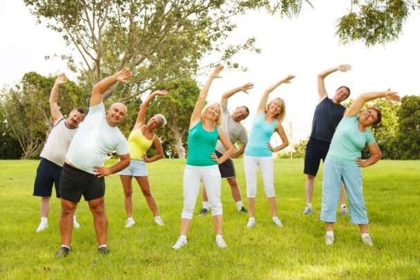 Groepje mannen en vrouwen doet oefeningen op een grasveld.