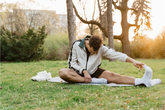 Man doet stretch oefeningen op een grasveld.