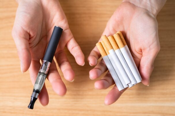 Een hand met sigaretten en een hand met een vape.
