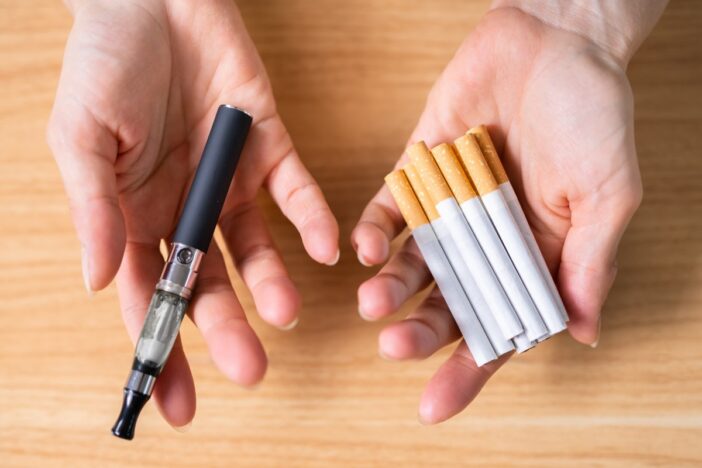 Een hand met sigaretten en een hand met een vape.