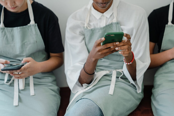 Drie mensen met een schort om maken gebruik van hun smartphone.
