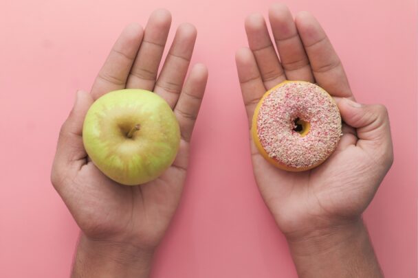 Hand met appel en hand met donut erop.