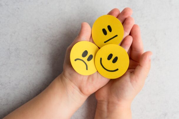 Drie papieren smileys in de handpalmen van een vrouw.