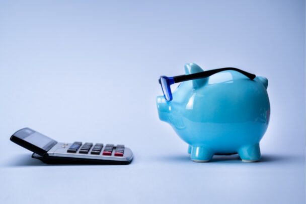 Blauw spaarvarken met bril kijkt naar een rekenmachine.
