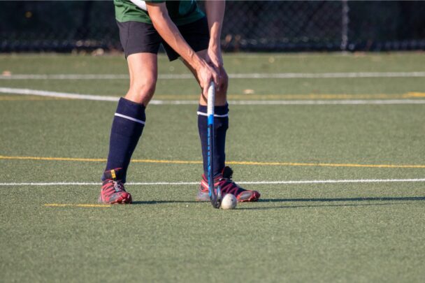 Man speelt hockey op grasveld en paast de bal.