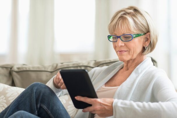 Vrouw zit op de bank en gebruikt een tablet.