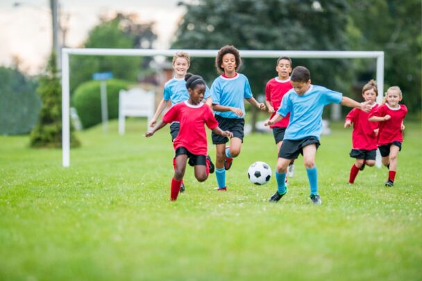Kinderen spelen potje voetbal op een grasveld.