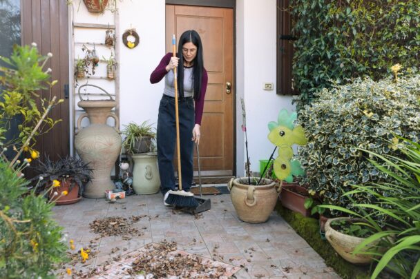 Vrouw veegt bladeren van haar stoepje schoon.