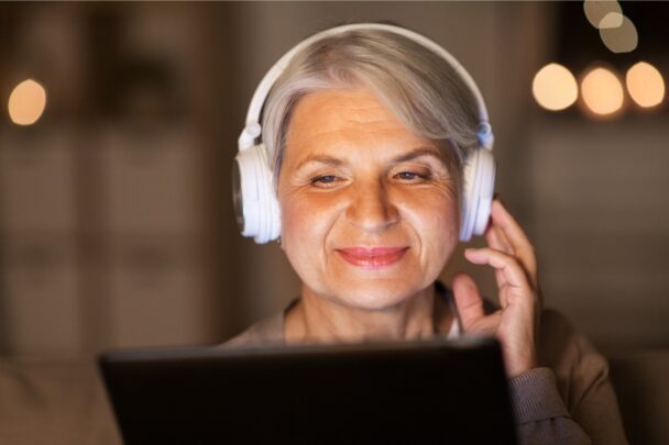 Oudere dame luistert naar muziek met een koptelefoon. Ze lacht.