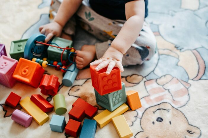 Jong kind speelt op een kleed met gekleurde blokjes.