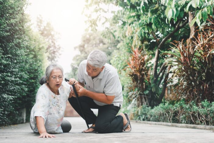 Oudere vrouw gevallen op straat. Ze wordt geholpen door een oudere man.