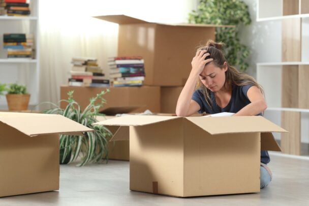 Vrouw zit met handen in het haar tussen stapels verhuisdozen.