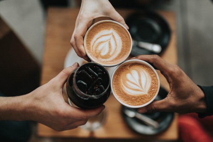 Drie handen proosten met koffie.
